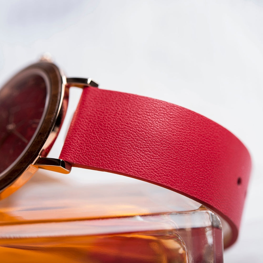 Close-up of a vibrant red leather watch strap attached to a wristwatch, highlighting its fine textured grain and sturdy connection to the metal casing.