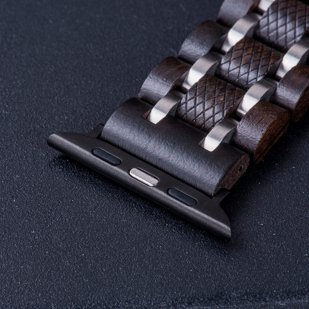 Close-up of a dark wooden watch band with metallic accents, featuring a textured design and durable clasp, laying on a black surface.