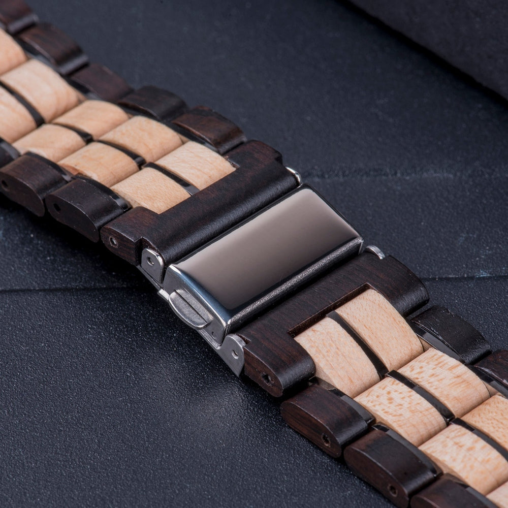 Close-up of a two-tone wooden watch band with dark and light wood links, featuring a polished silver clasp, displayed on a dark surface.