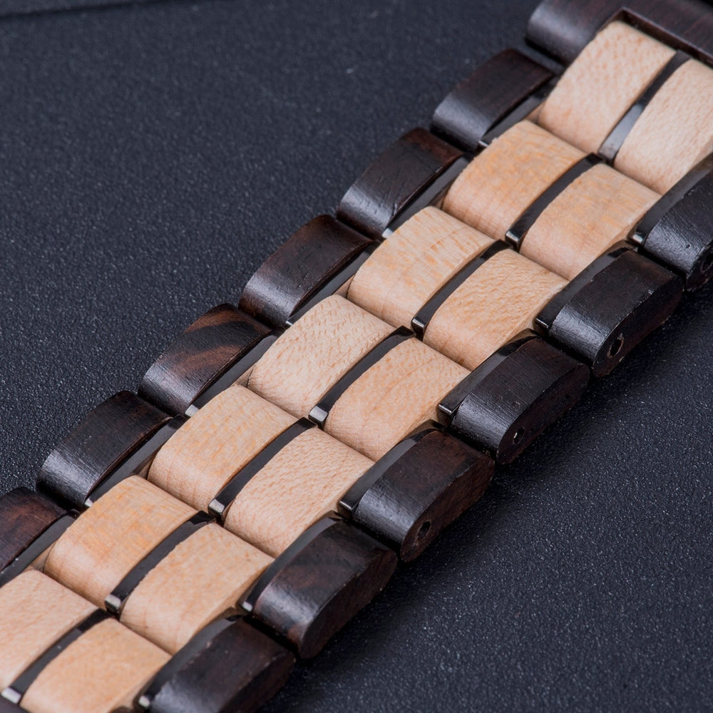 Close-up of a two-tone wooden watch band with alternating dark and light wood links, displaying detailed craftsmanship on a dark surface.