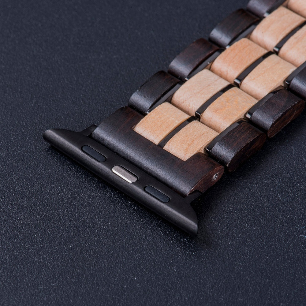 Close-up of a two-tone wooden watch band with dark and light wood links, featuring a black clasp connector, displayed on a dark surface.