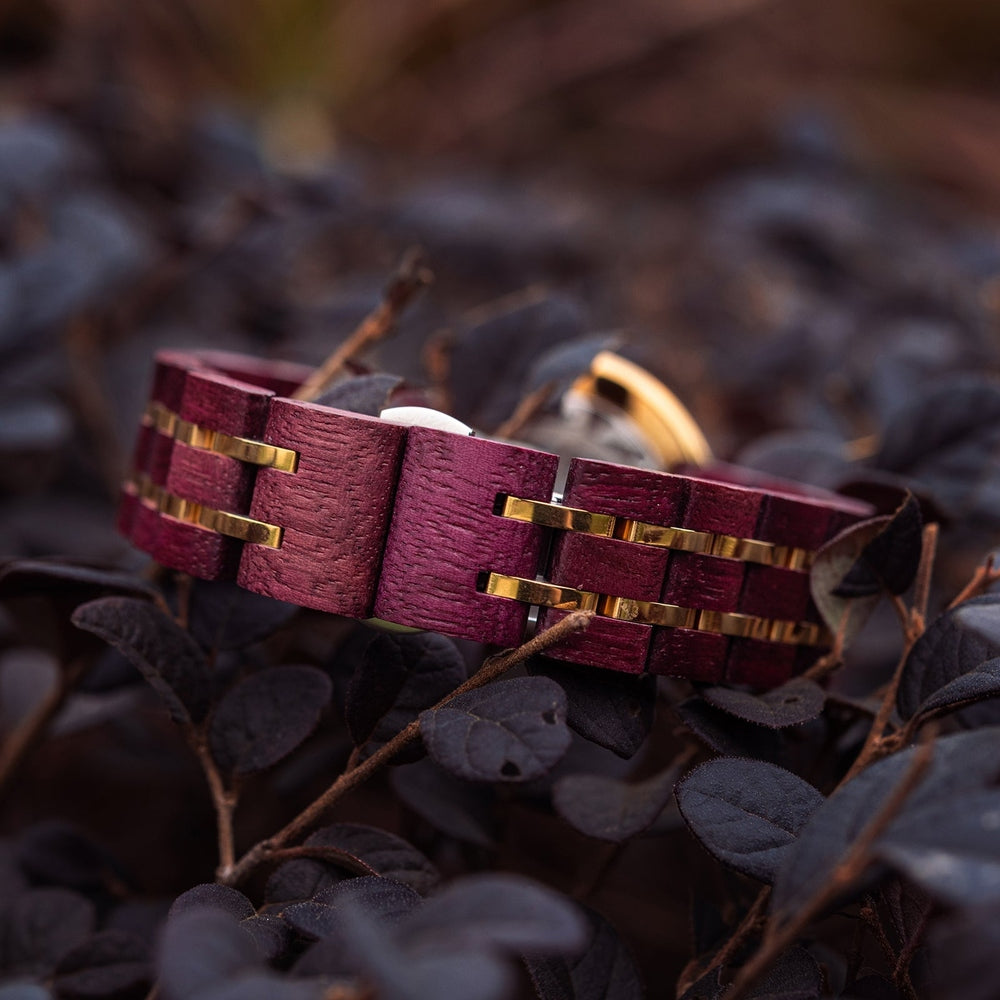 Close-up of the red Mokozai wooden wristwatch band featuring intricate gold accents, elegantly resting on dark foliage for a natural contrast.
