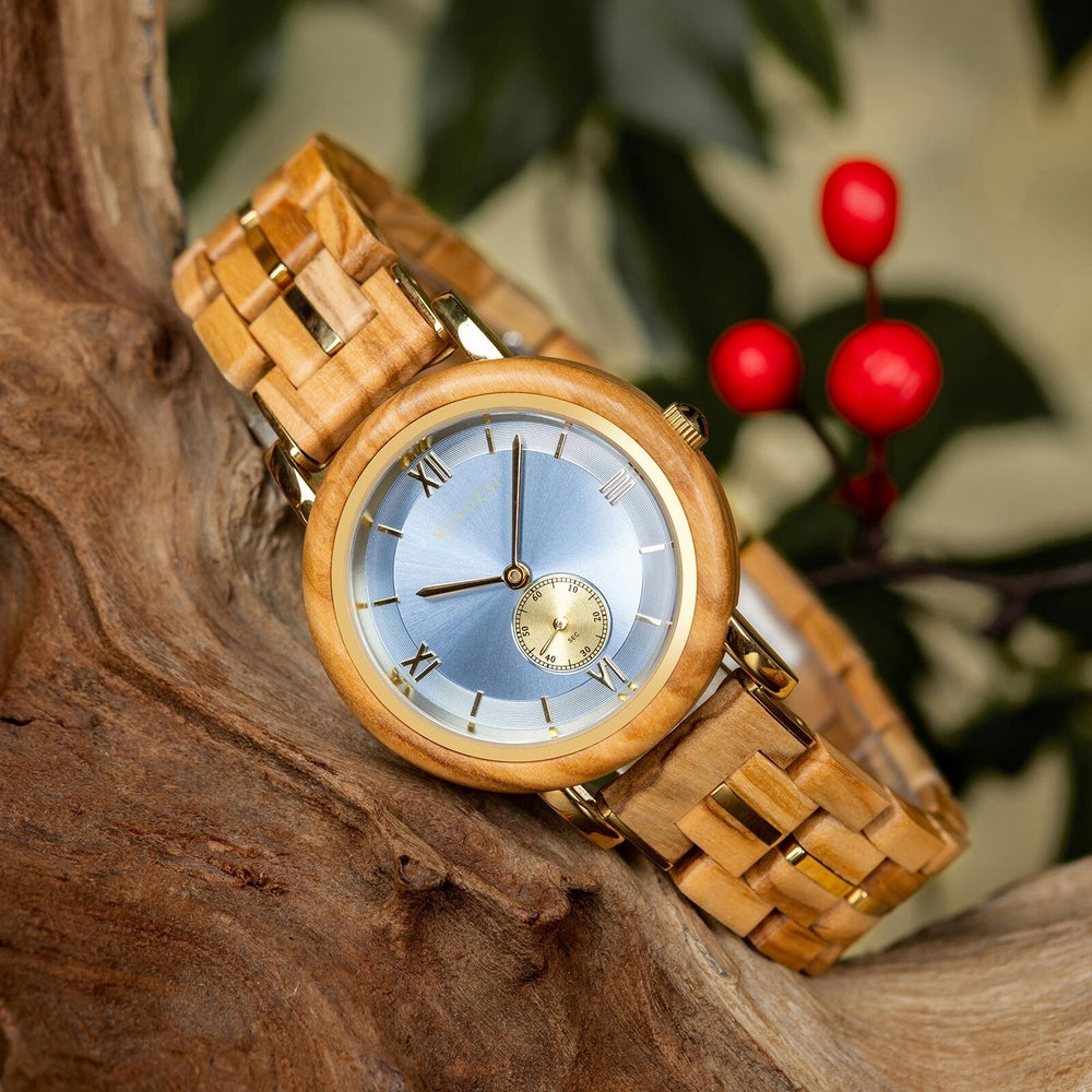 Sophisticated Mokozai wooden wristwatch with a light wood band, gold details, and a light blue dial featuring Roman numerals and a subdial, elegantly displayed on a piece of driftwood with vibrant red berries and green leaves in the background.