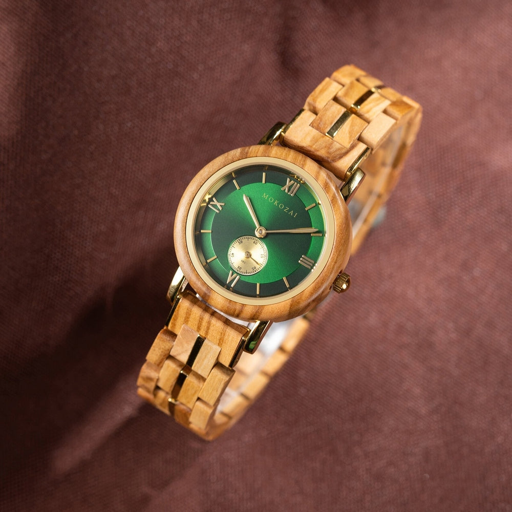 Mokozai handcrafted wooden wristwatch with a green dial, Roman numeral markers, and gold accents, set against a brown fabric backdrop, showcasing its natural elegance and luxury craftsmanship.