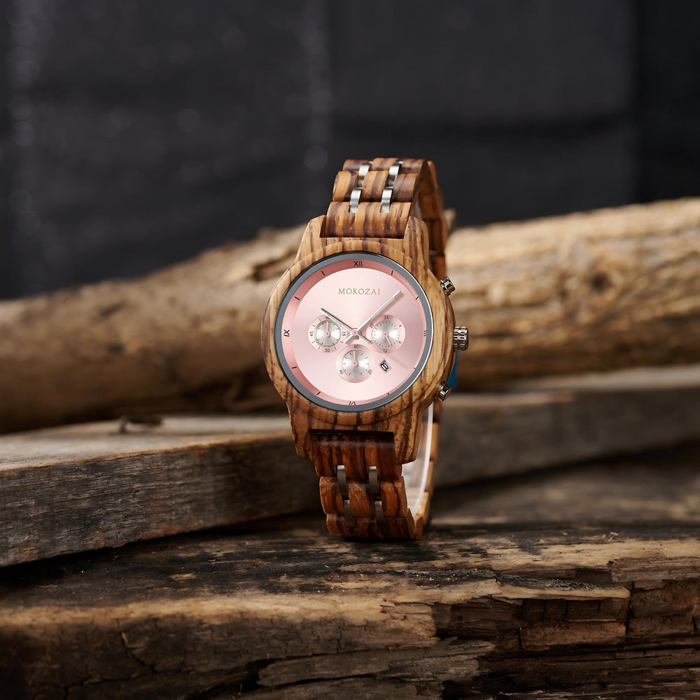 A Mokozai wooden wristwatch featuring a pink dial with silver subdials and Roman numeral markers, displayed on a rustic wooden surface.