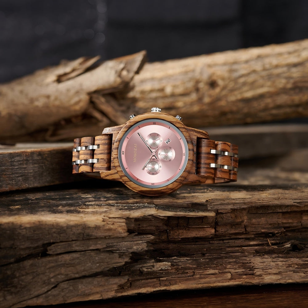 Front view of a Mokozai wooden wristwatch with a pink dial, featuring silver chronograph subdials and Roman numeral markers, set on a rustic wooden background.
