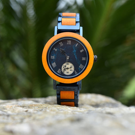 Mokozai wristwatch with a vibrant orange wood bezel and black Roman numeral dial, featuring a small subdial at 6 o'clock. The band incorporates matching orange wood inlays, set against a backdrop of natural greenery, combining a bold, eco-friendly design with timeless elegance. Ideal for eco-conscious individuals in Australia looking for unique, sustainable fashion accessories.