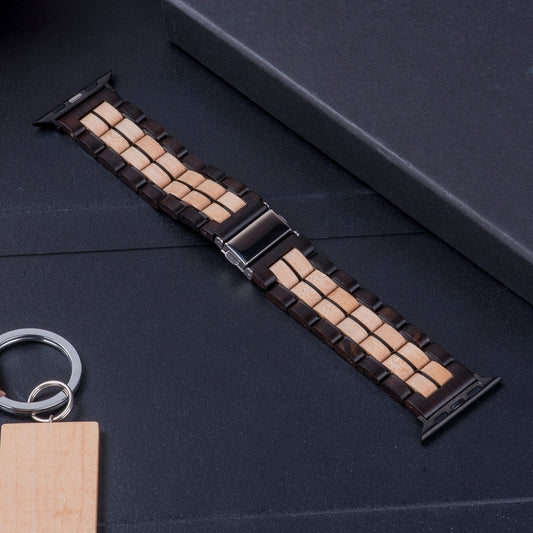 Two-tone wooden watch band with dark and light wood links, featuring a silver clasp, displayed on a black surface with a wooden keychain in the background.