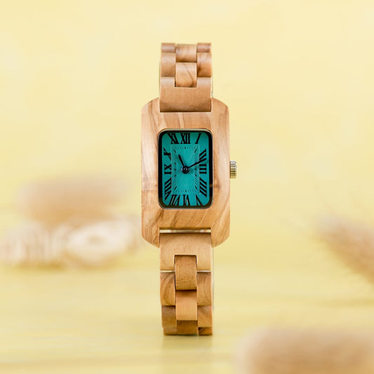 Elegant Mokozai wooden watch with a square teal dial and bold Roman numerals, complemented by a light wooden strap, set against a soft yellow background.