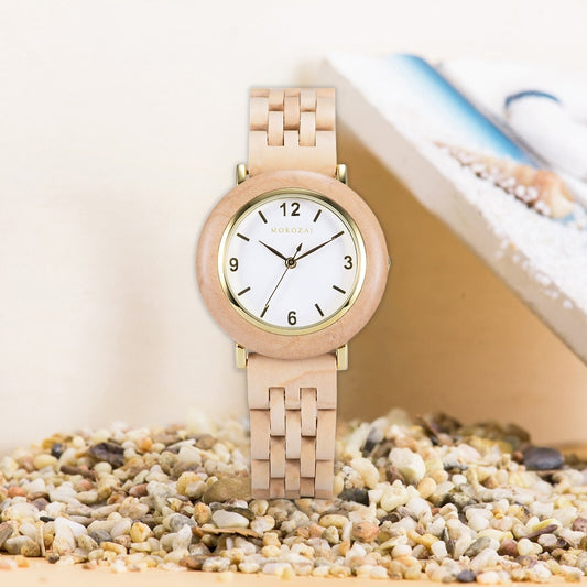 Mokozai wooden wristwatch featuring a minimalist white dial with black numerals, encased in a light wood bezel and gold accents, displayed on a bed of smooth pebbles for a natural, beach-inspired look.