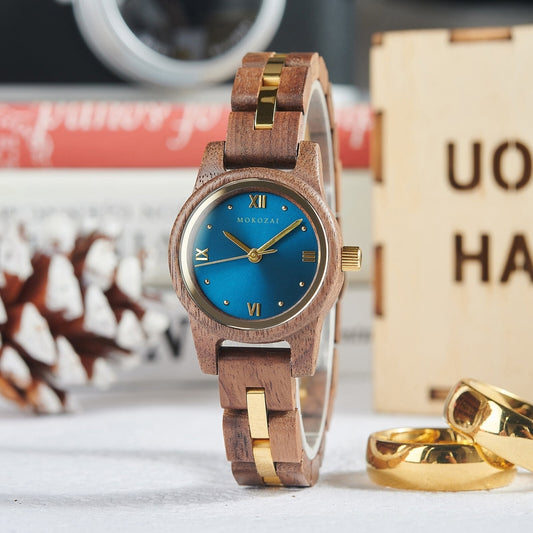 Mokozai wooden wristwatch with a rich brown wood band and gold accents, featuring a striking blue dial with Roman numerals, beautifully displayed with gold rings and a festive pinecone in the background.