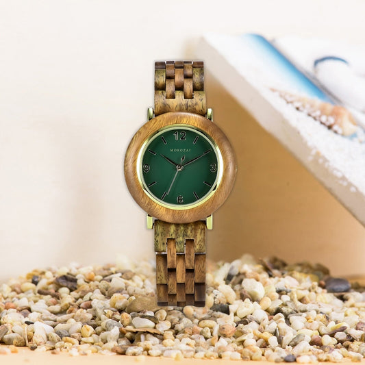Mokozai wooden wristwatch with a smooth natural wood frame, green dial, and woven wooden strap, displayed on a bed of pebbles. The watch exudes a rustic, nature-inspired elegance, ideal for eco-conscious fashion enthusiasts in Australia.