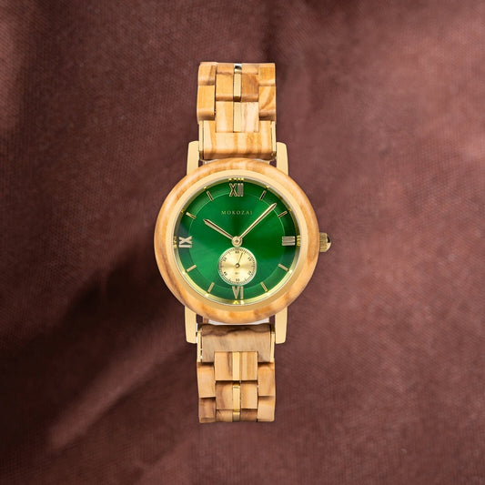 Mokozai wooden wristwatch featuring a green dial with Roman numerals and a gold-tone subdial, set against a rich brown fabric backdrop, highlighting its elegant and natural design.