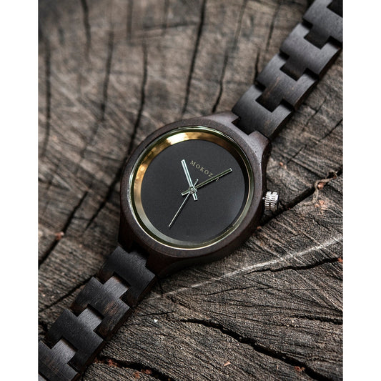 Mokozai minimalist black wooden wristwatch with gold accents, placed on a textured tree trunk surface. The sleek, eco-friendly design emphasizes natural wood and sustainable style, appealing to Australian shoppers seeking refined, nature-inspired timepieces.