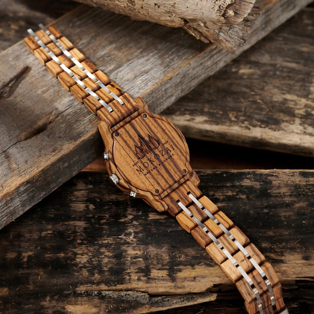 Back view of a wooden wristwatch displaying Mokozai branding and nature-inspired engraving, paired with a wood and silver-tone link strap, set on a rustic wooden background.